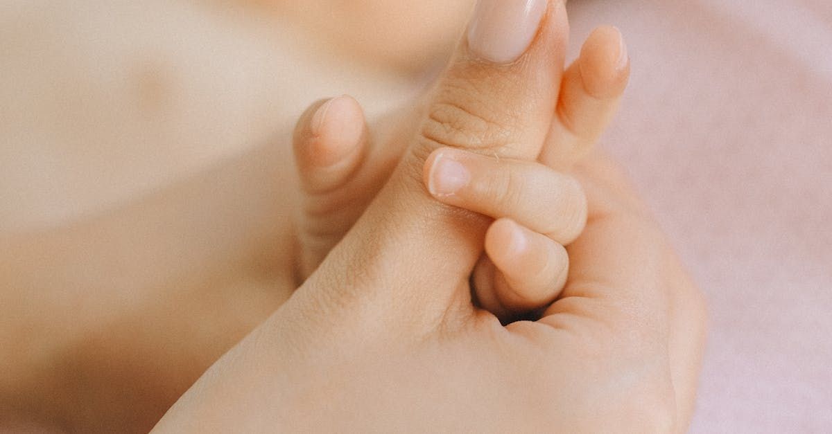 An adult hand holding a baby's tiny hand, pink background.