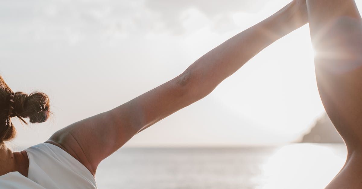Woman doing yoga on beach, arms raised, sunlight, sea in background.