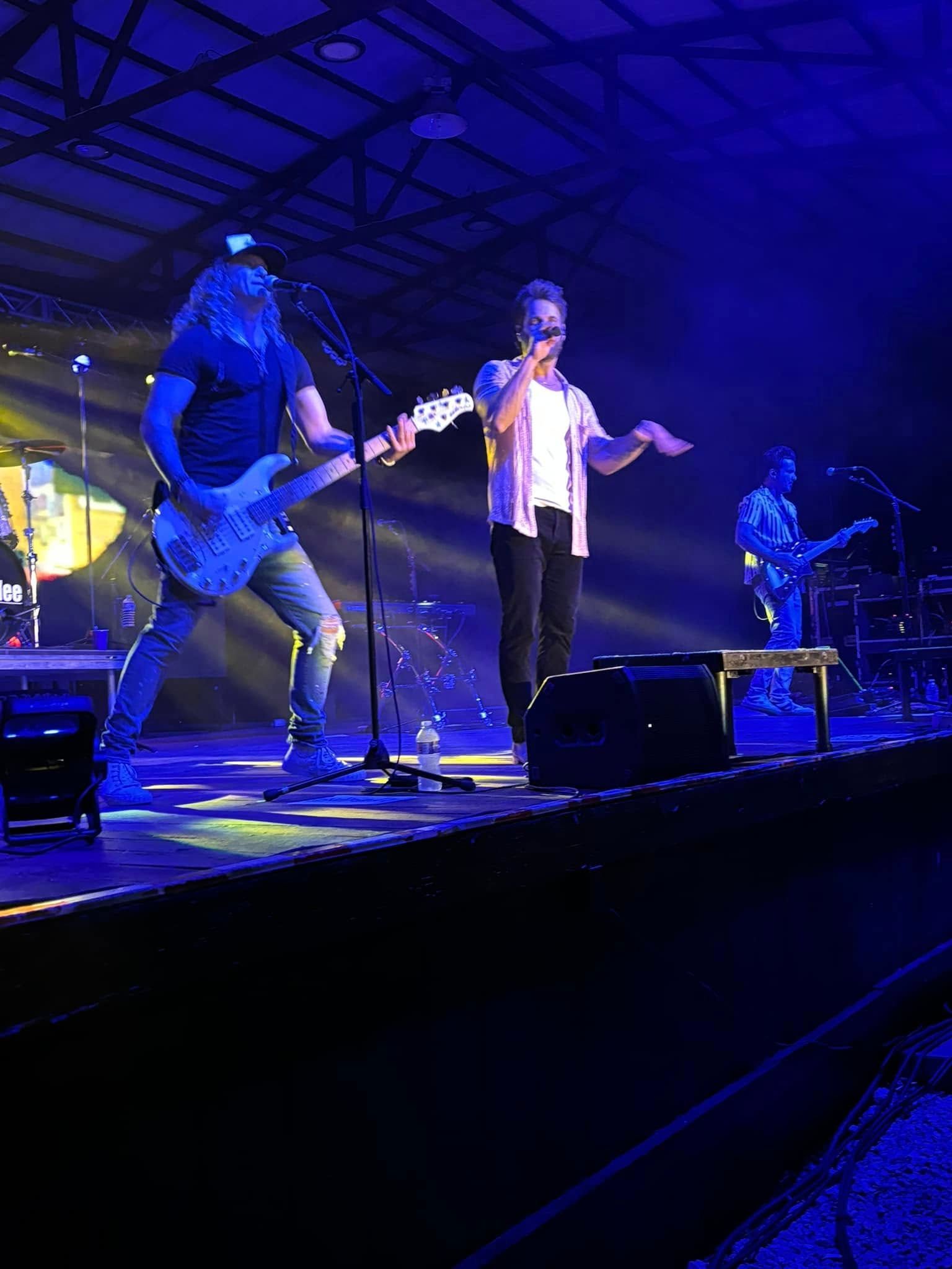Live band performing on a blue-lit stage, with a singer at center and guitarist at left.