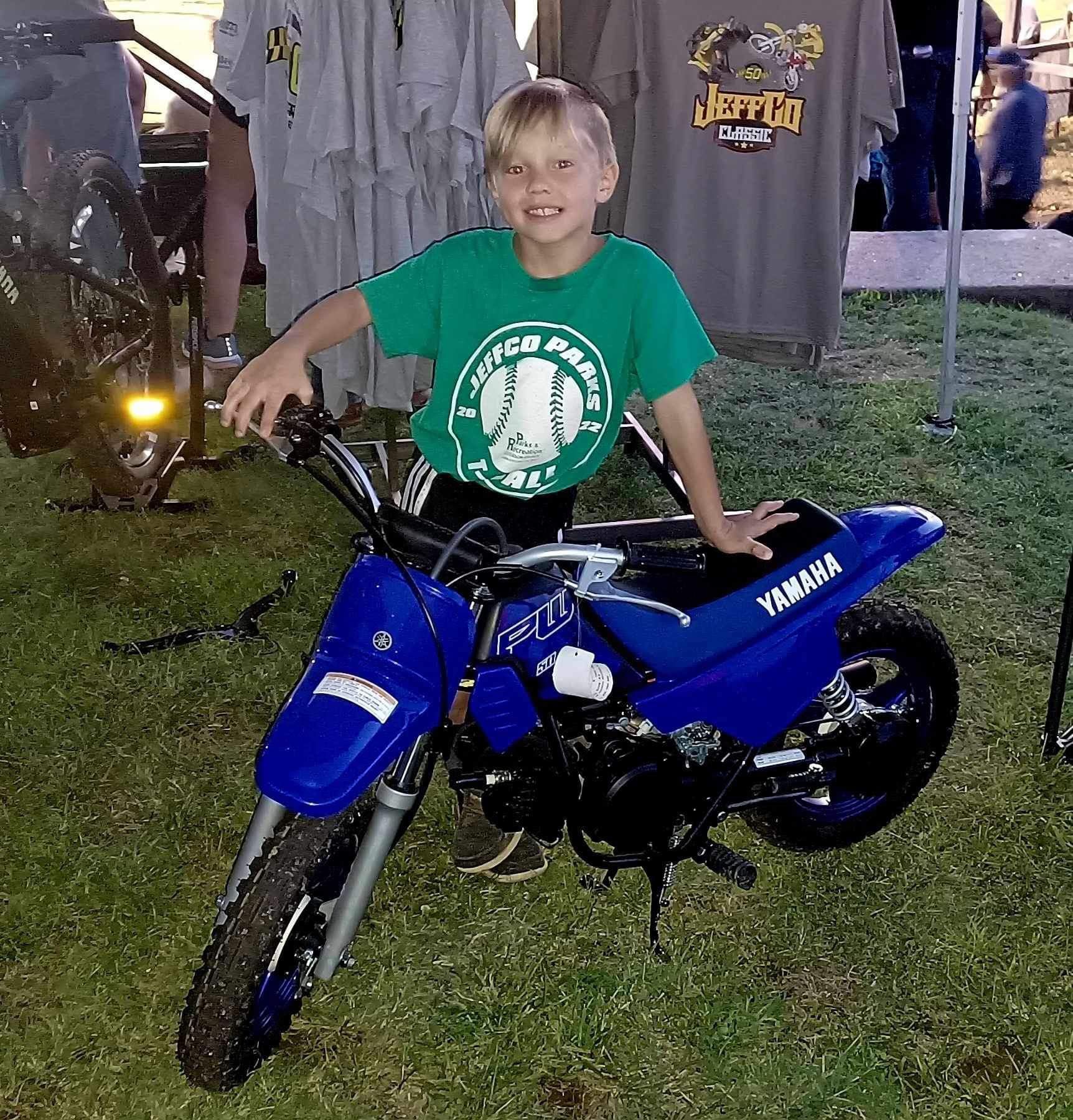 Child smiling on a blue Yamaha dirt bike at an outdoor event at night