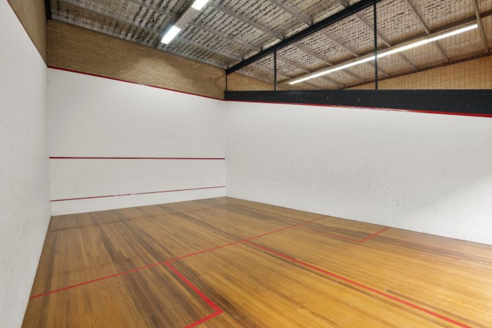 An empty squash court with a wooden floor and white walls.