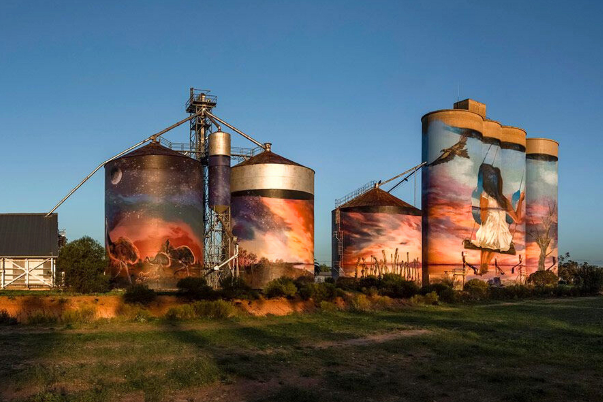 A group of silos with paintings on them in a field.
