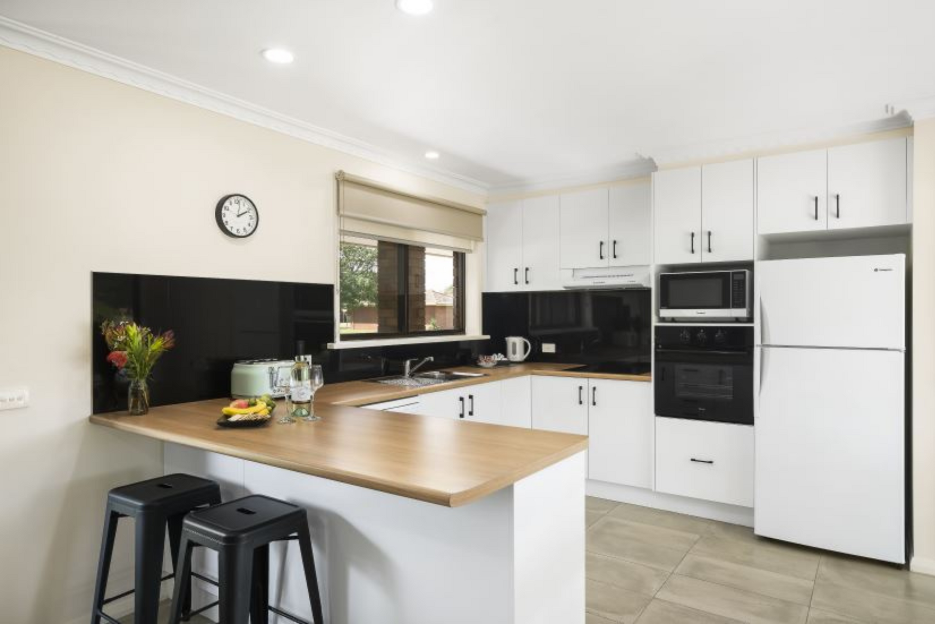 A kitchen with white cabinets and black stools and a clock on the wall.