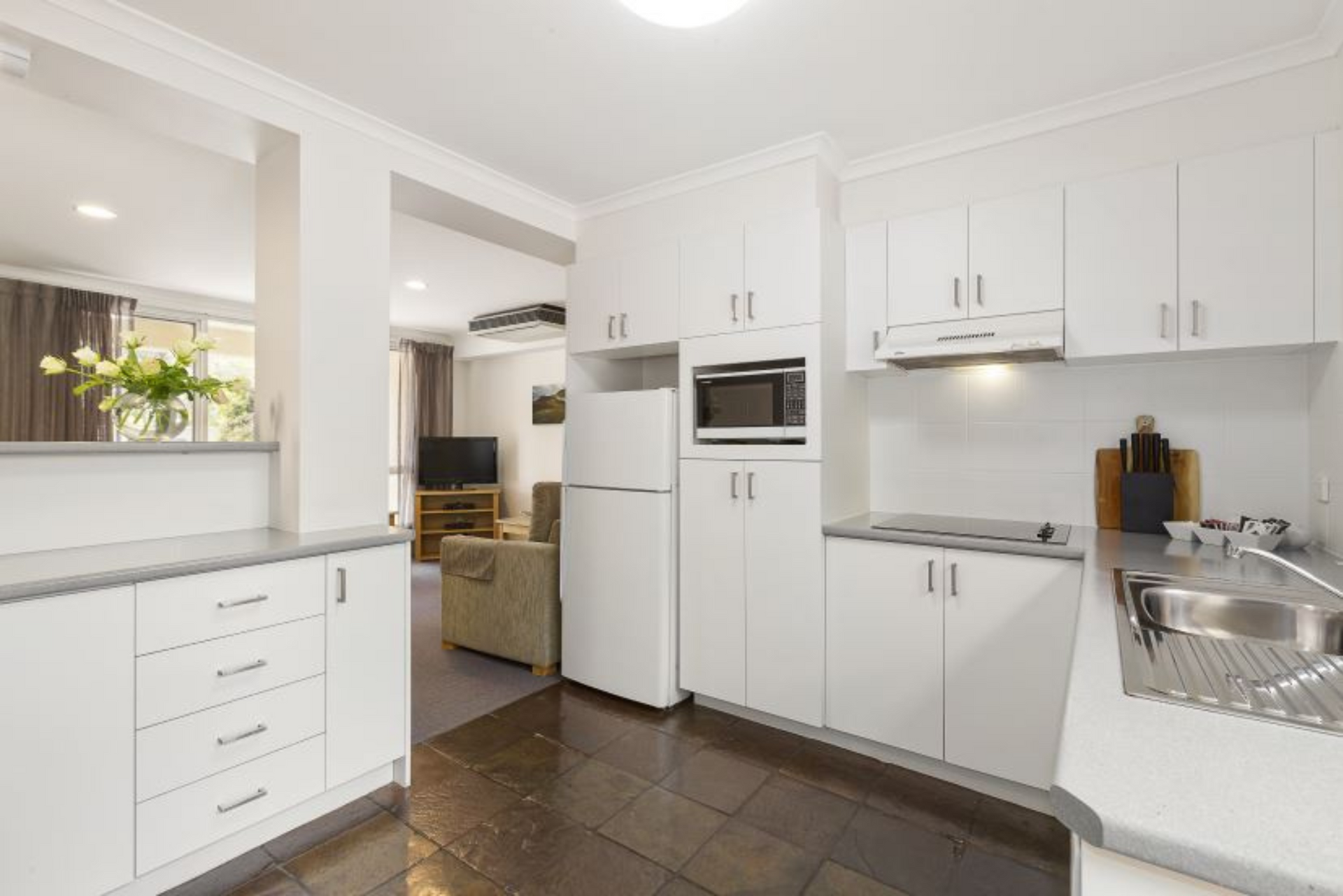 A kitchen with white cabinets , a refrigerator , a microwave , and a sink.