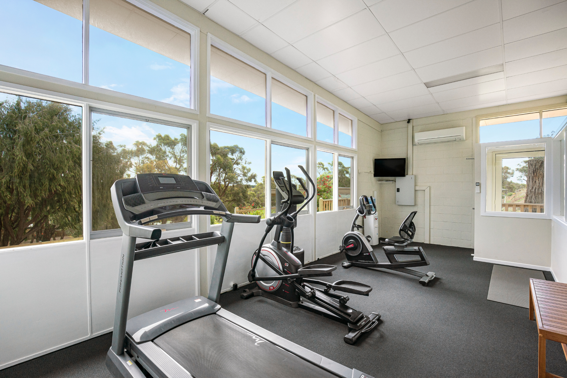 A gym with treadmills , ellipticals , and a television.