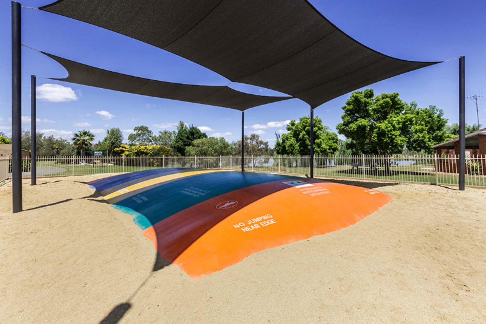 A rainbow colored jumping pillow in a park under a canopy.