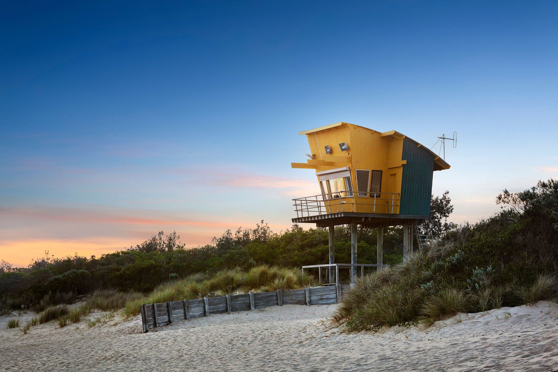 A yellow lifeguard tower is sitting on top of a sandy beach.