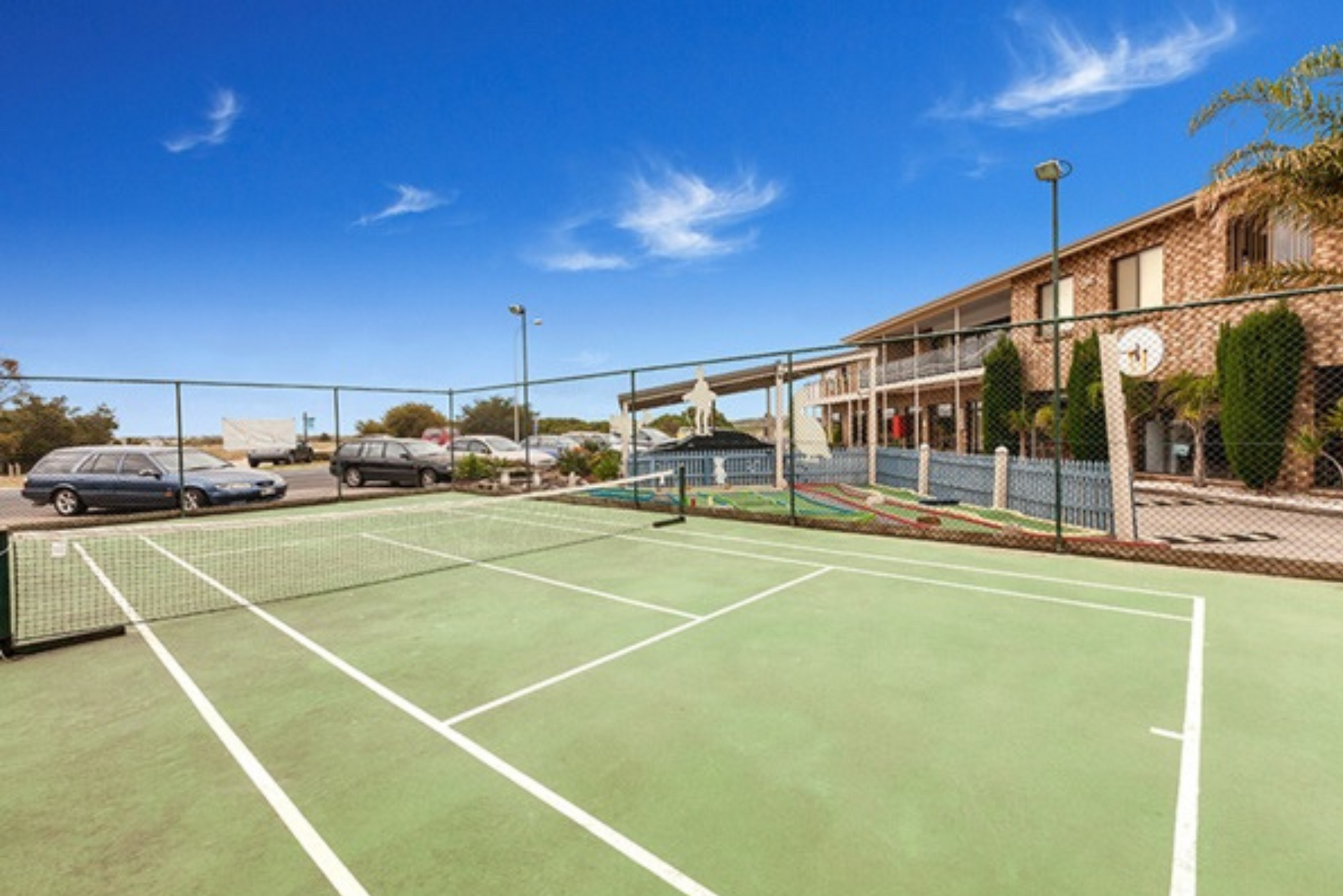 A tennis court with a basketball hoop in front of a building.