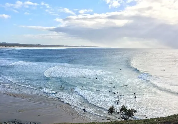 A group of people are surfing on a beach in the ocean.