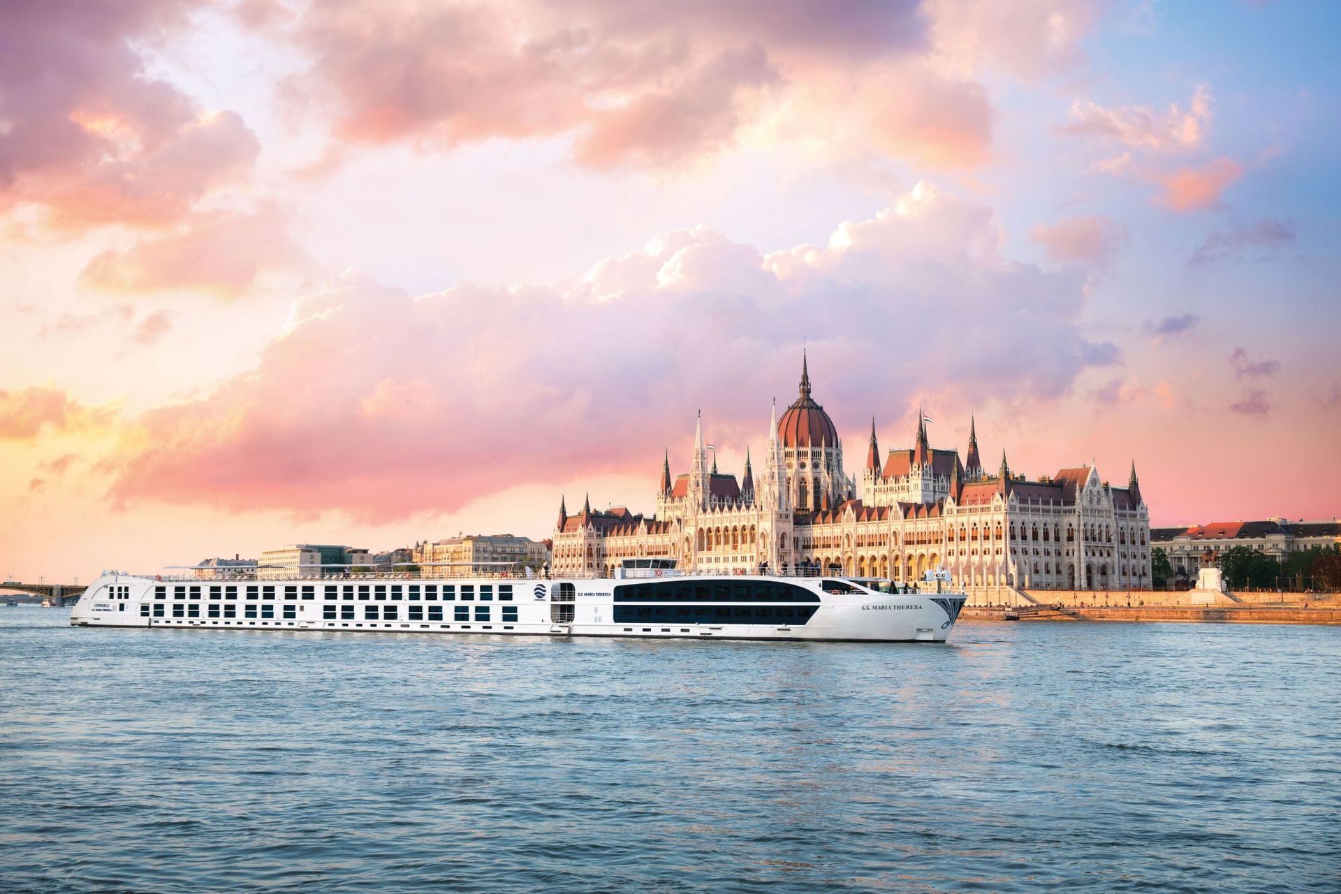 S.S. Maria Theresa cruise ship on the Danube River in front of the Hungarian Parliament Building at sunset.