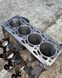 Bloque de motor de cuatro cilindros con cilindros expuestos y bielas, apoyado sobre hormigón.