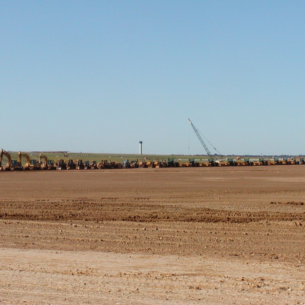 A row of construction vehicles are parked on a dirt field
