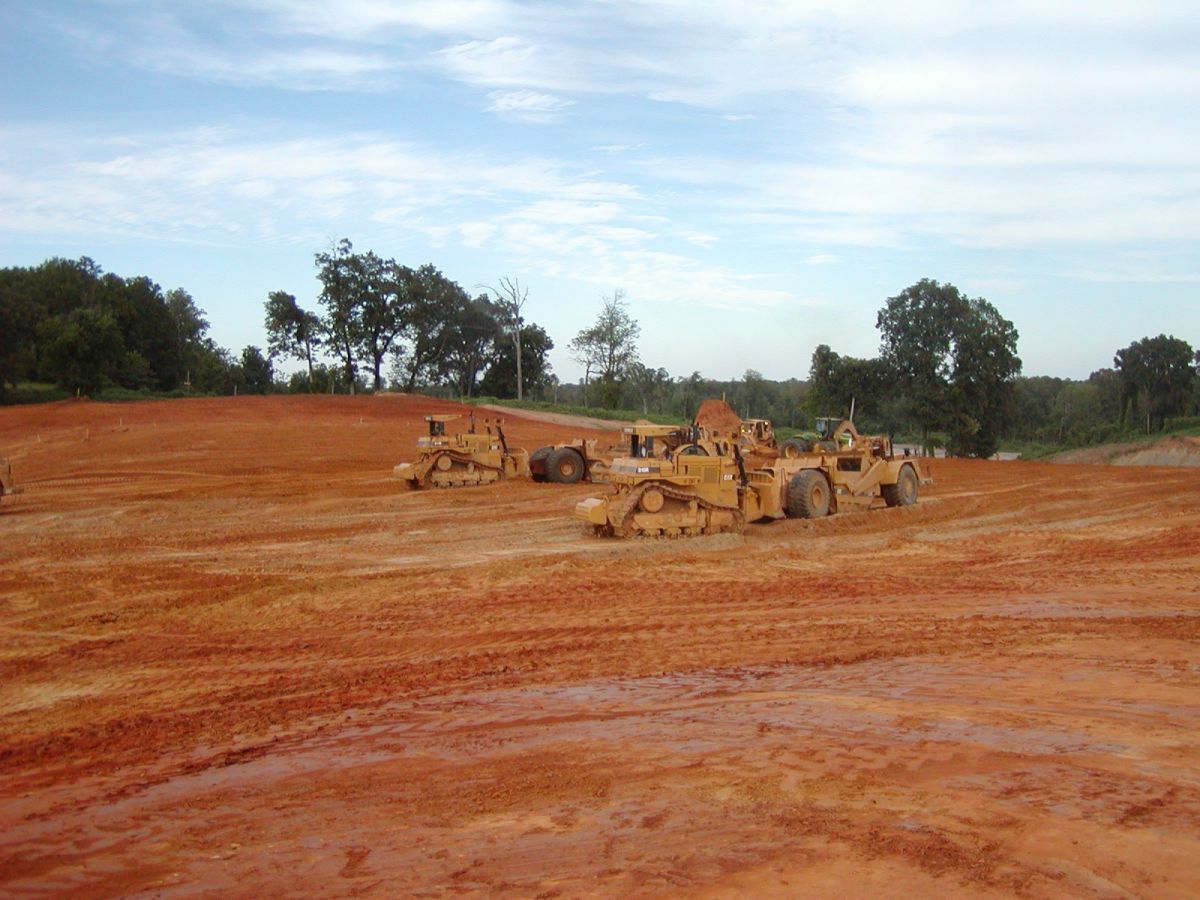 A group of construction vehicles are parked in a dirt field.
