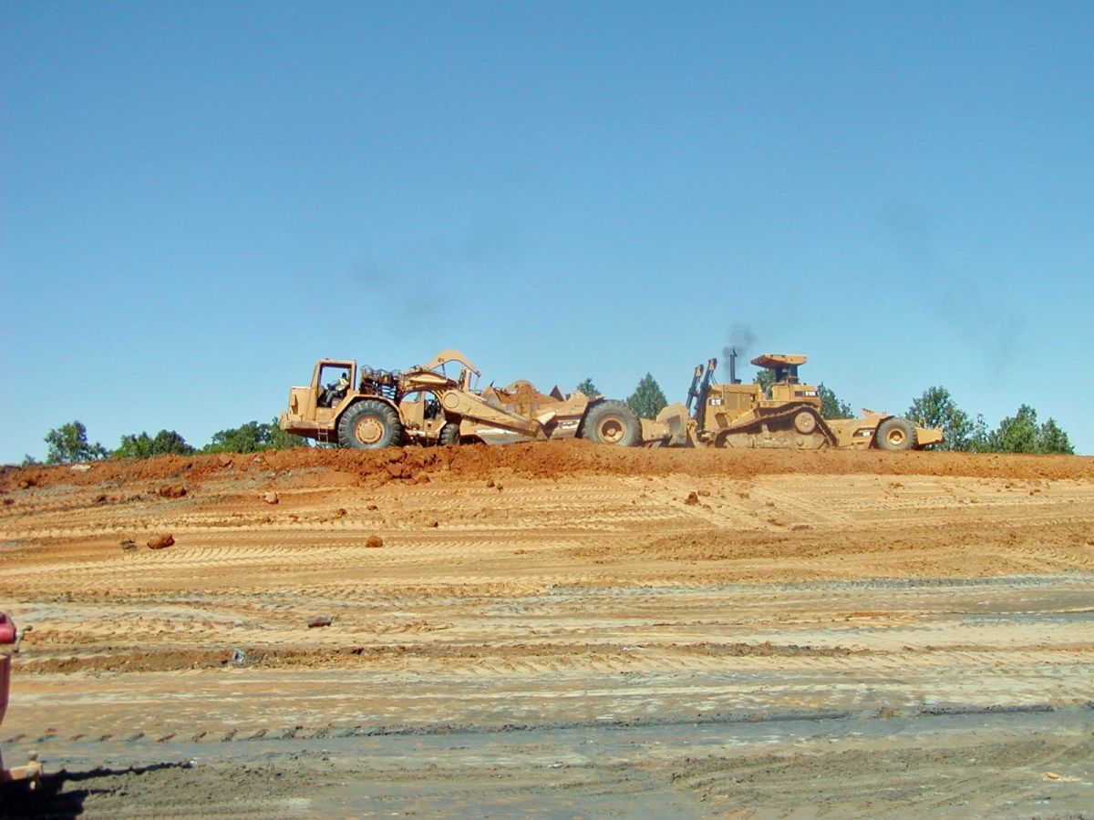 A couple of bulldozers are working on a dirt field