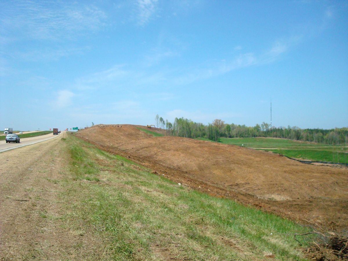 A dirt hill on the side of a highway next to a grassy field.