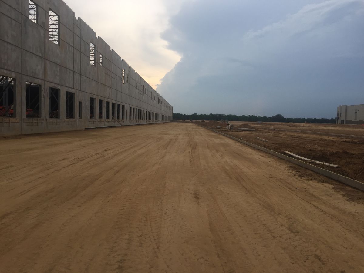 A dirt road leading to a large building under construction.