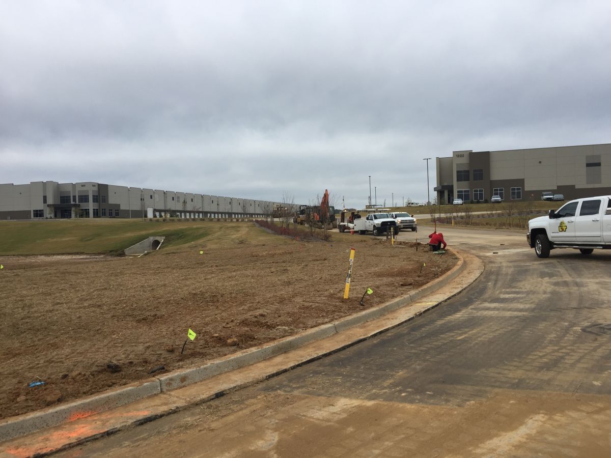 A white truck is parked on the side of a dirt road in front of a large building.