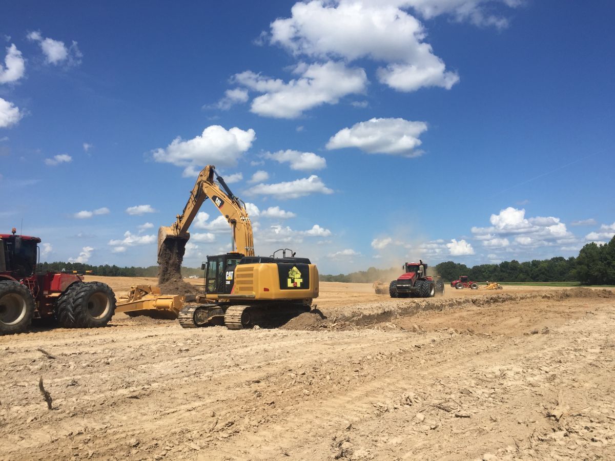 A group of construction vehicles are working on a dirt field.