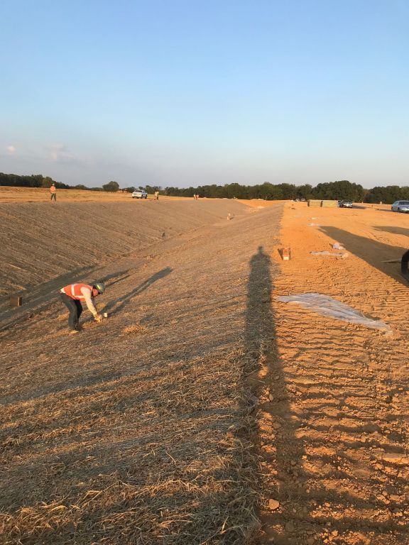 A man is working in a field with a tractor in the background.