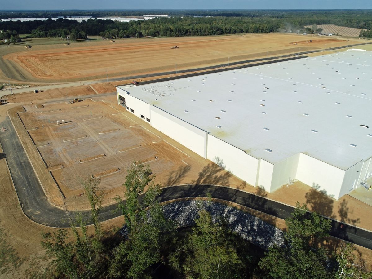 An aerial view of a large white building with a white roof surrounded by trees and dirt.