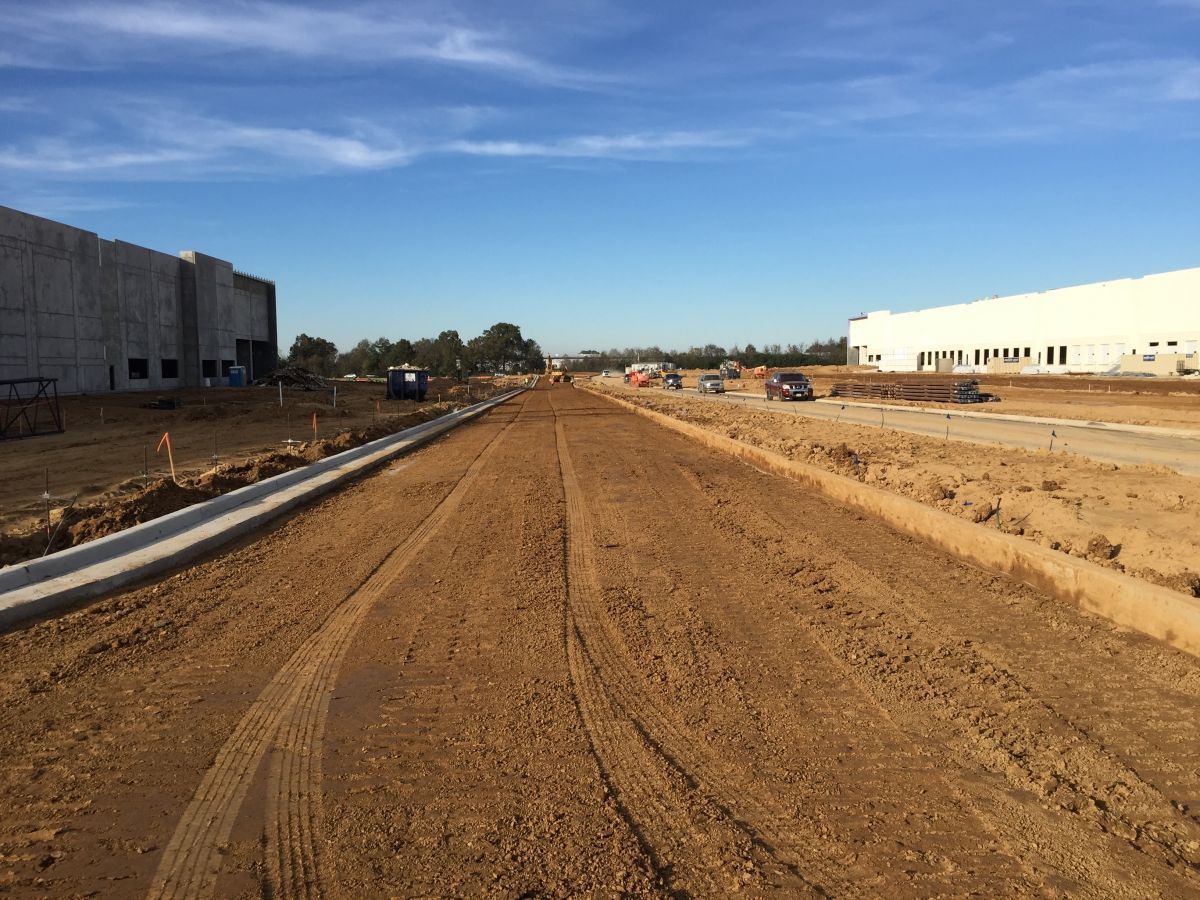 A dirt road going through a construction site with a building in the background.