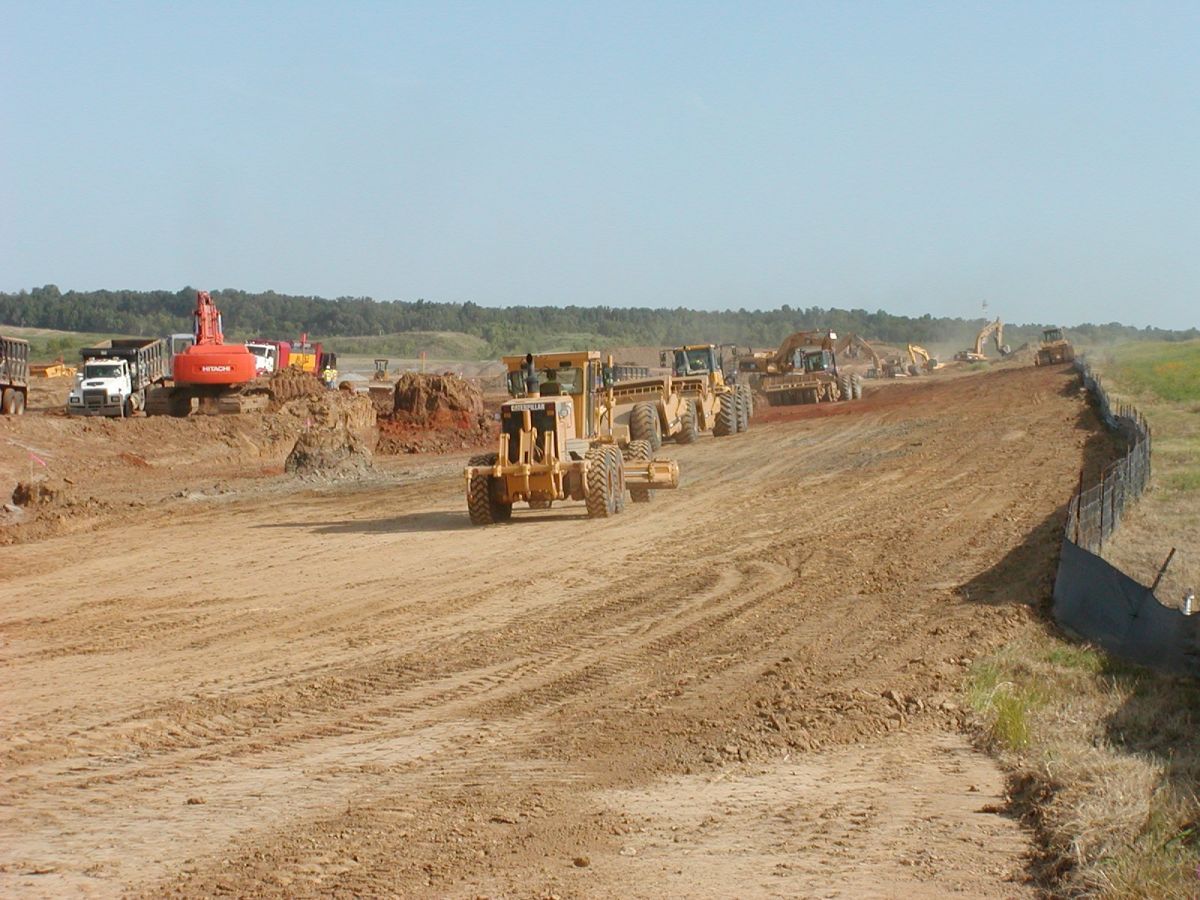 A group of construction vehicles are working on a dirt road.