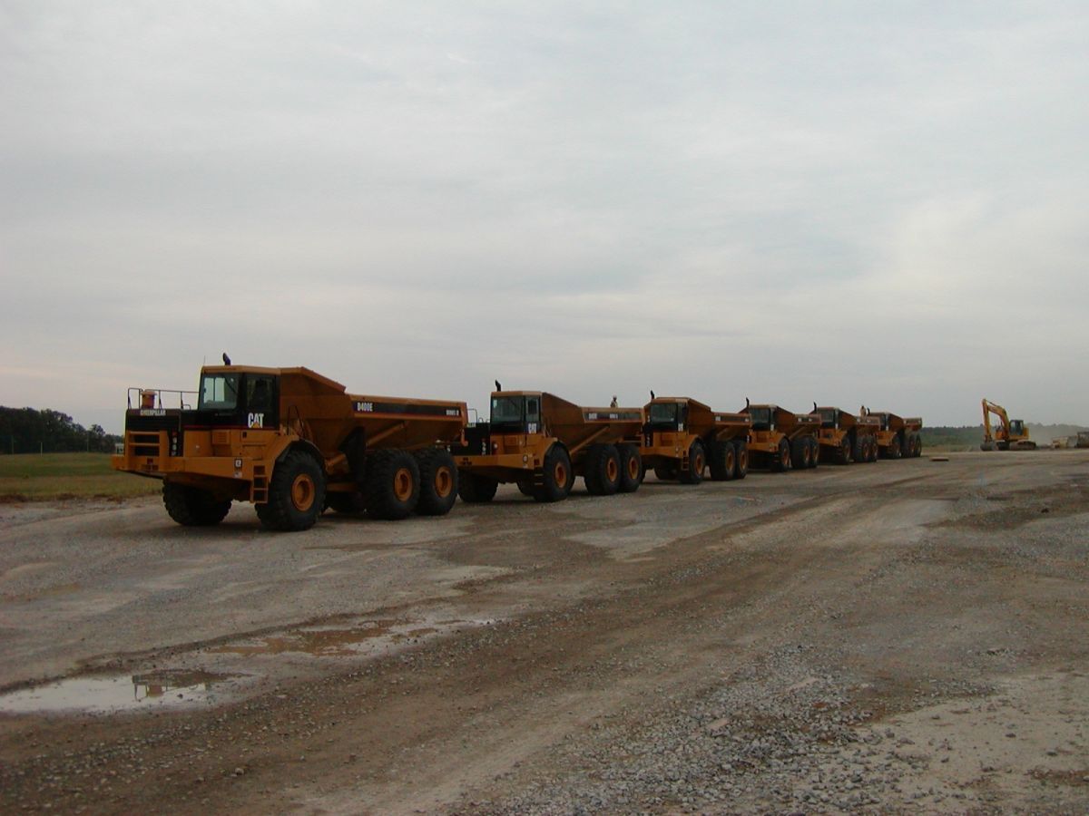 A row of dump trucks are parked on a dirt road