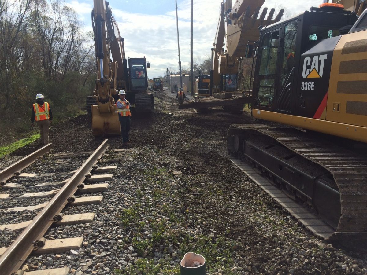 A cat excavator is on the side of a train track