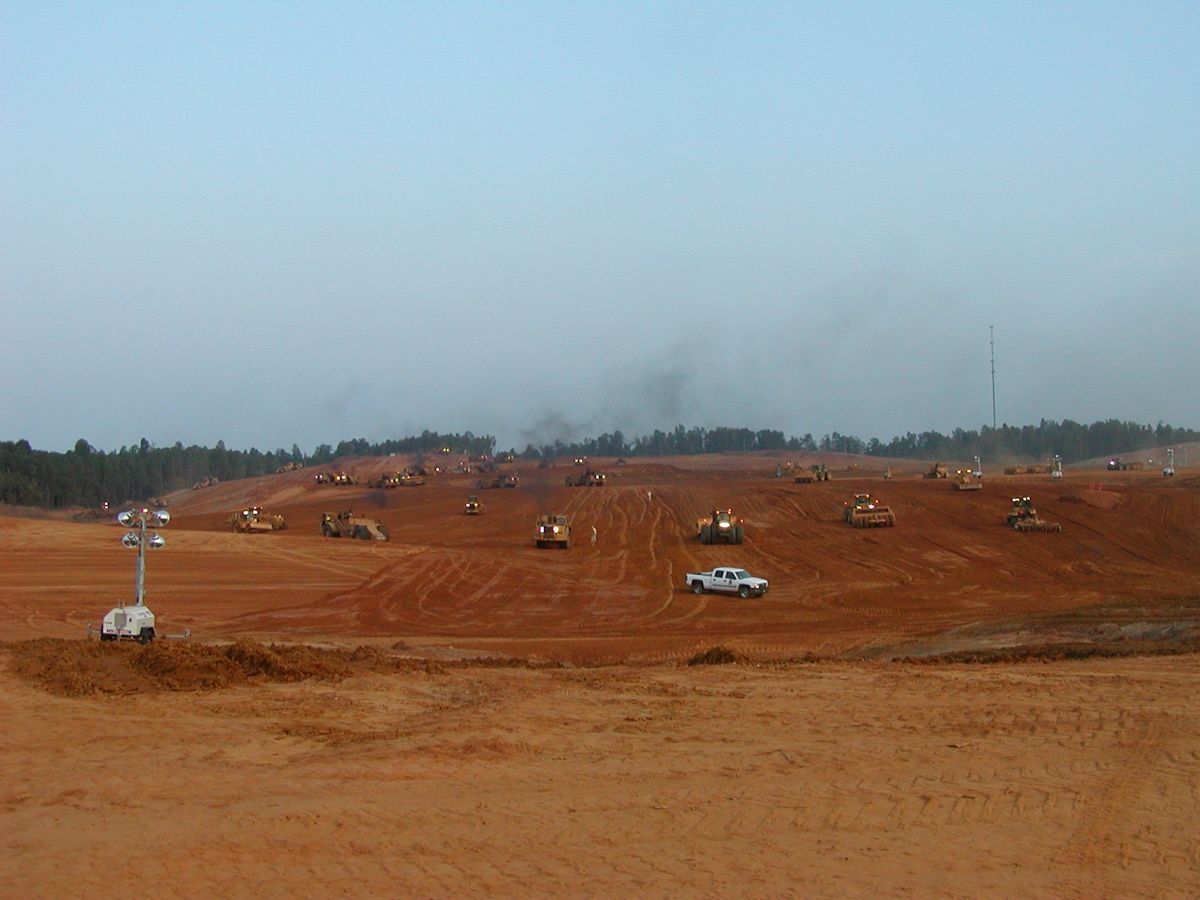 A group of construction vehicles are working on a dirt field.