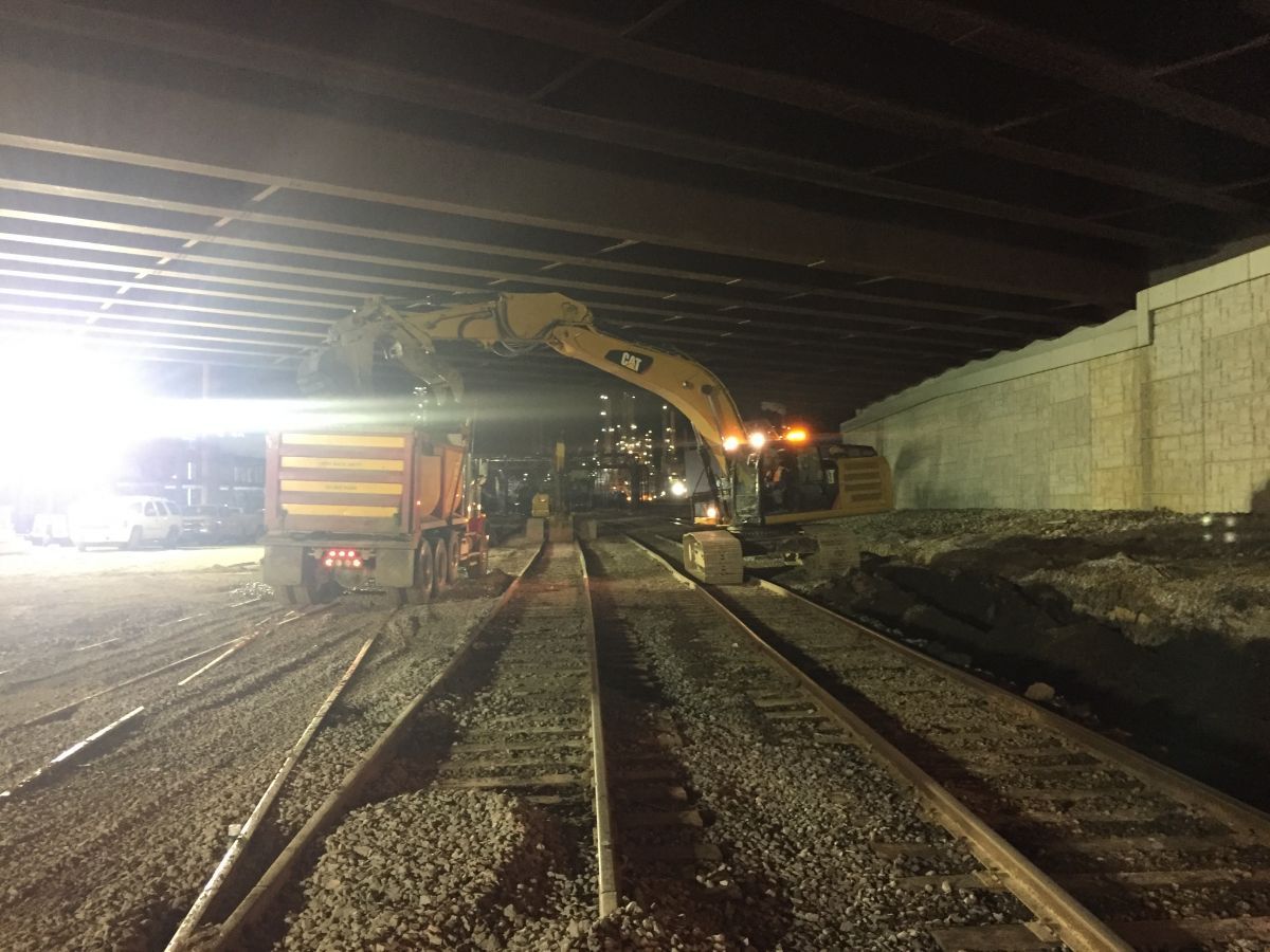 A large yellow excavator is working on train tracks at night.
