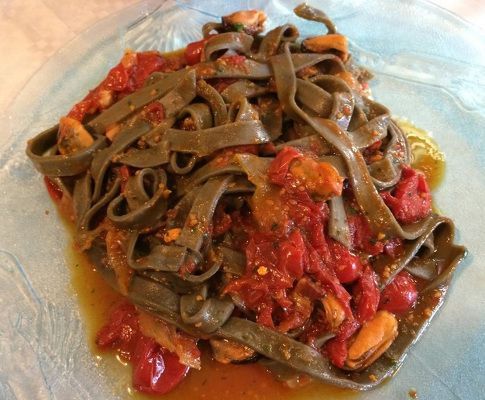 Piatto di pasta verde con sugo di pomodoro e frutti di mare.