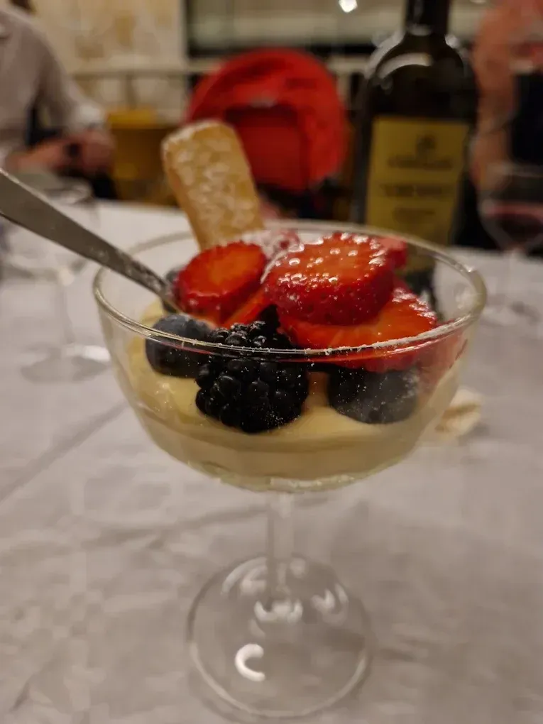 Dessert in un bicchiere con stelo: base cremosa guarnita con frutti di bosco e un biscotto
