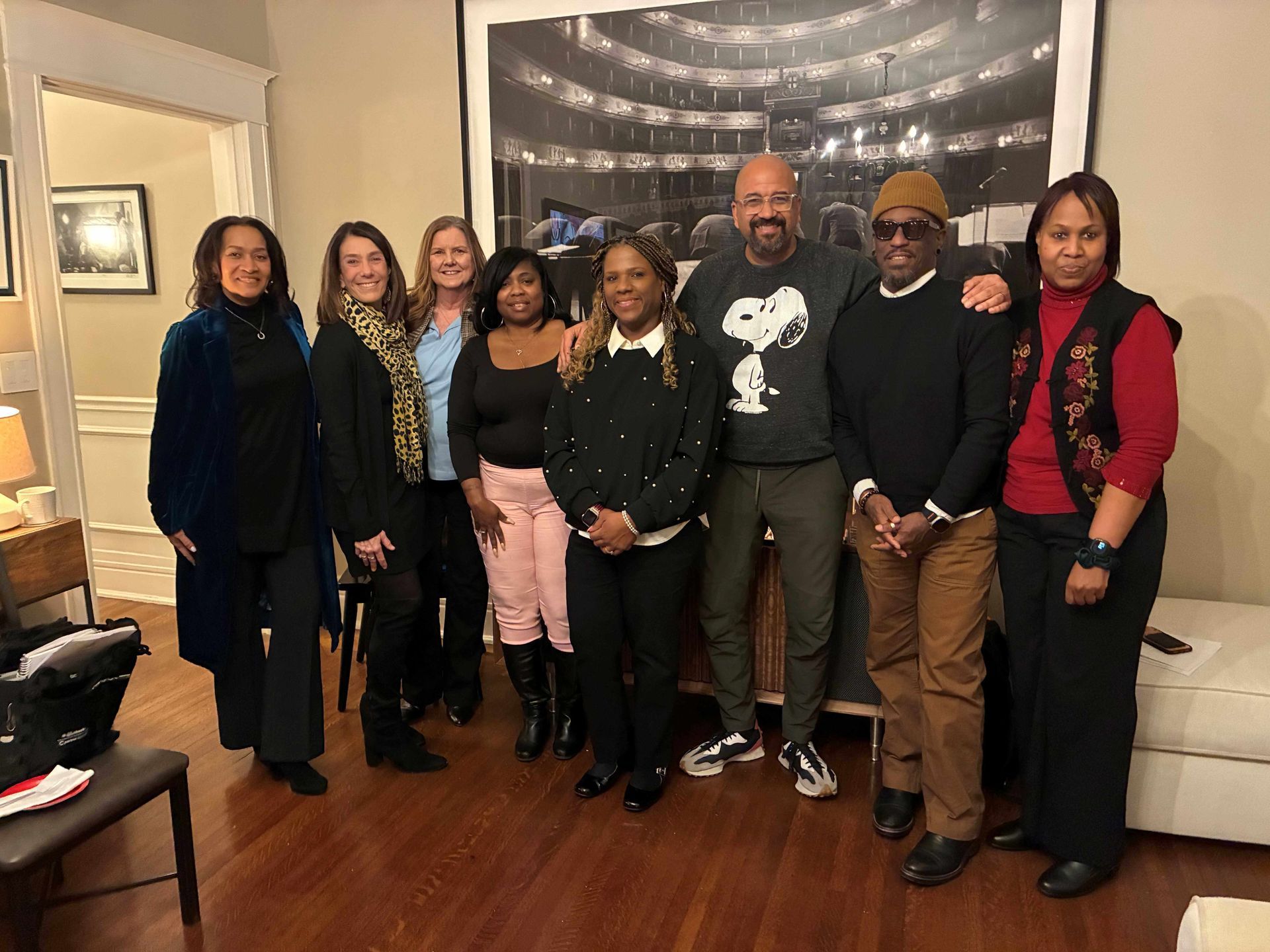 Group of people posing together in a room with a large photo on the wall.