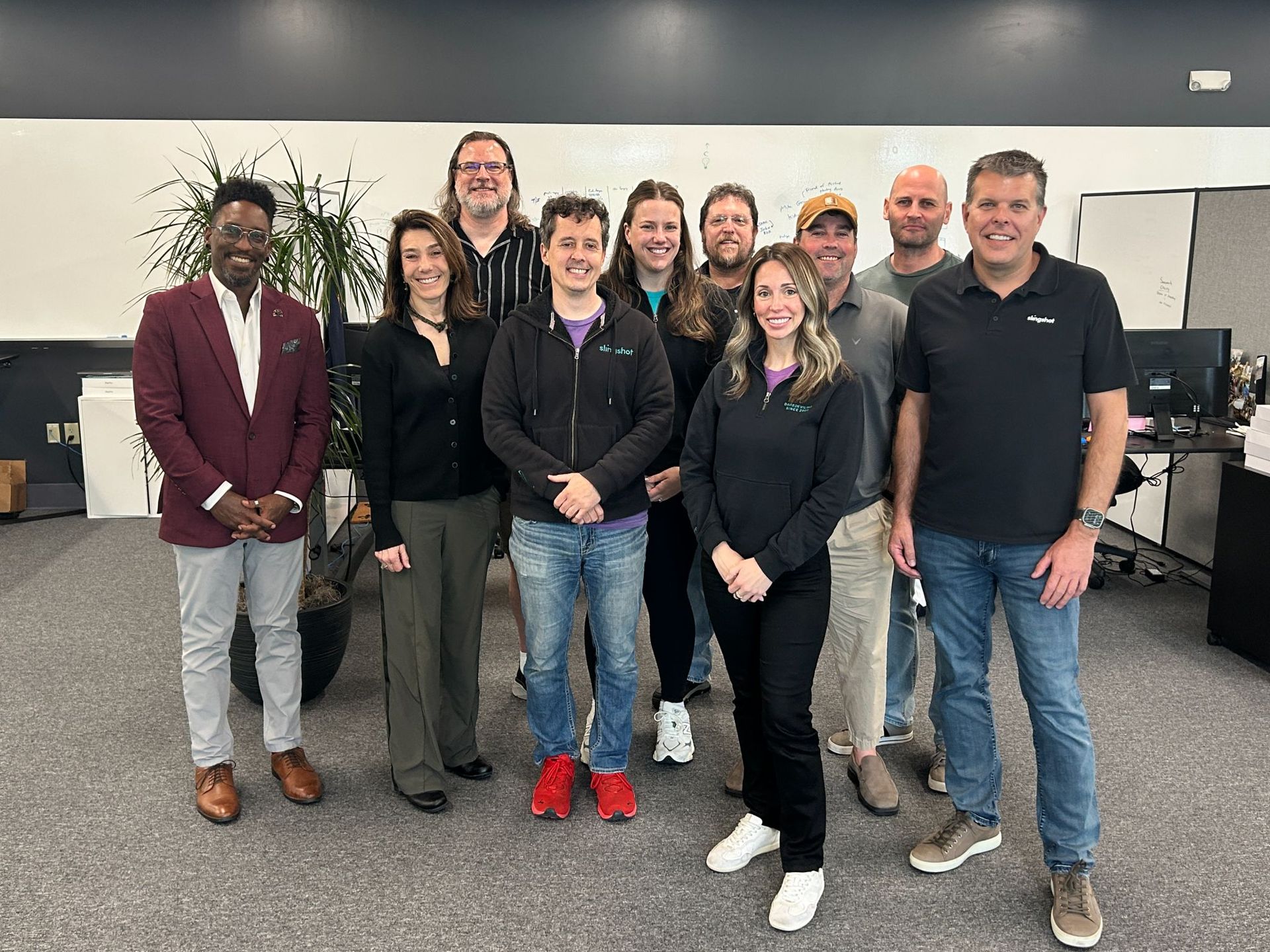 Group of people posing for a photo in an office. People are of various heights and wearing casual attire.