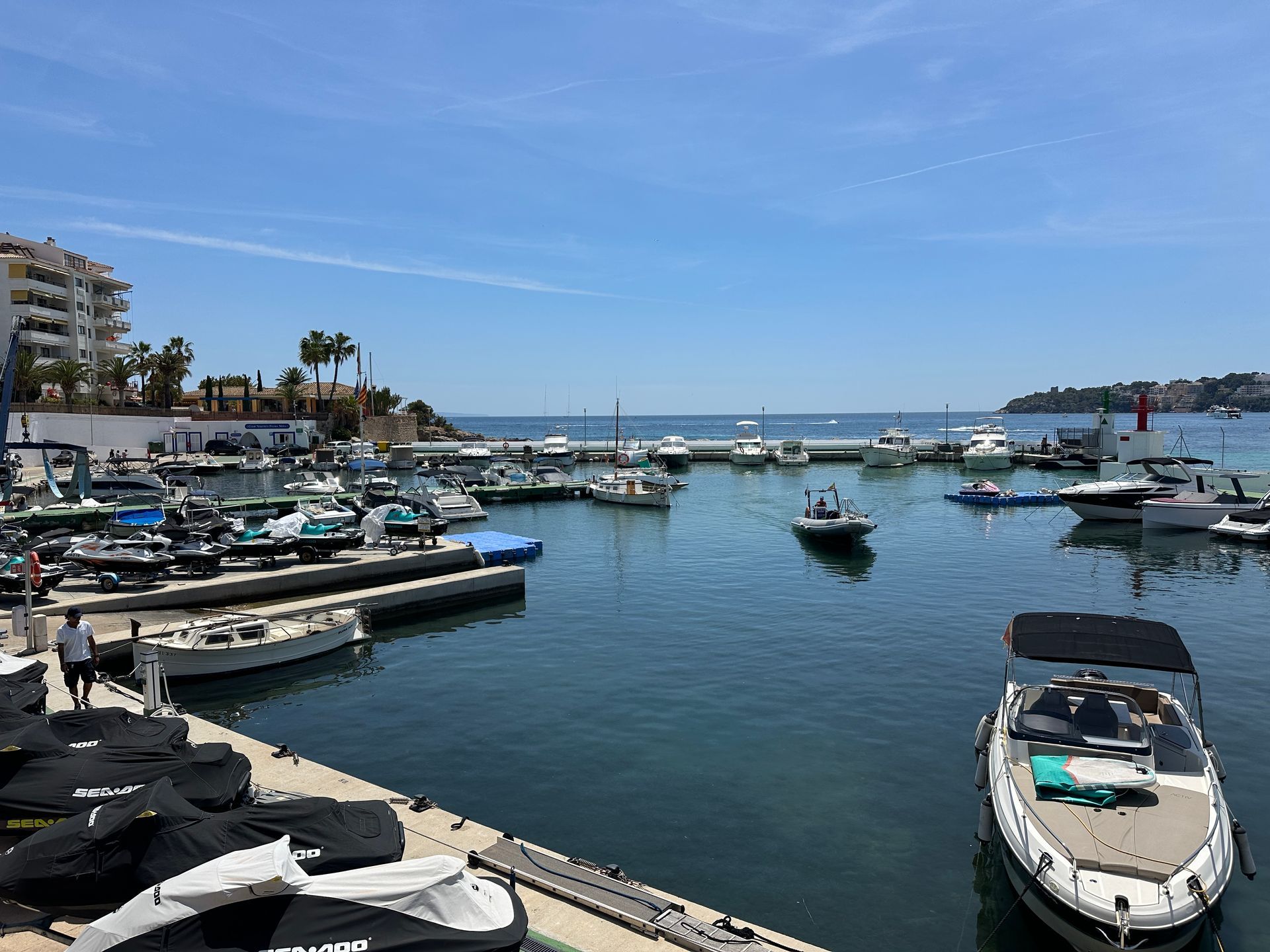 Un puerto deportivo lleno de barcos y motos de agua en un día soleado.