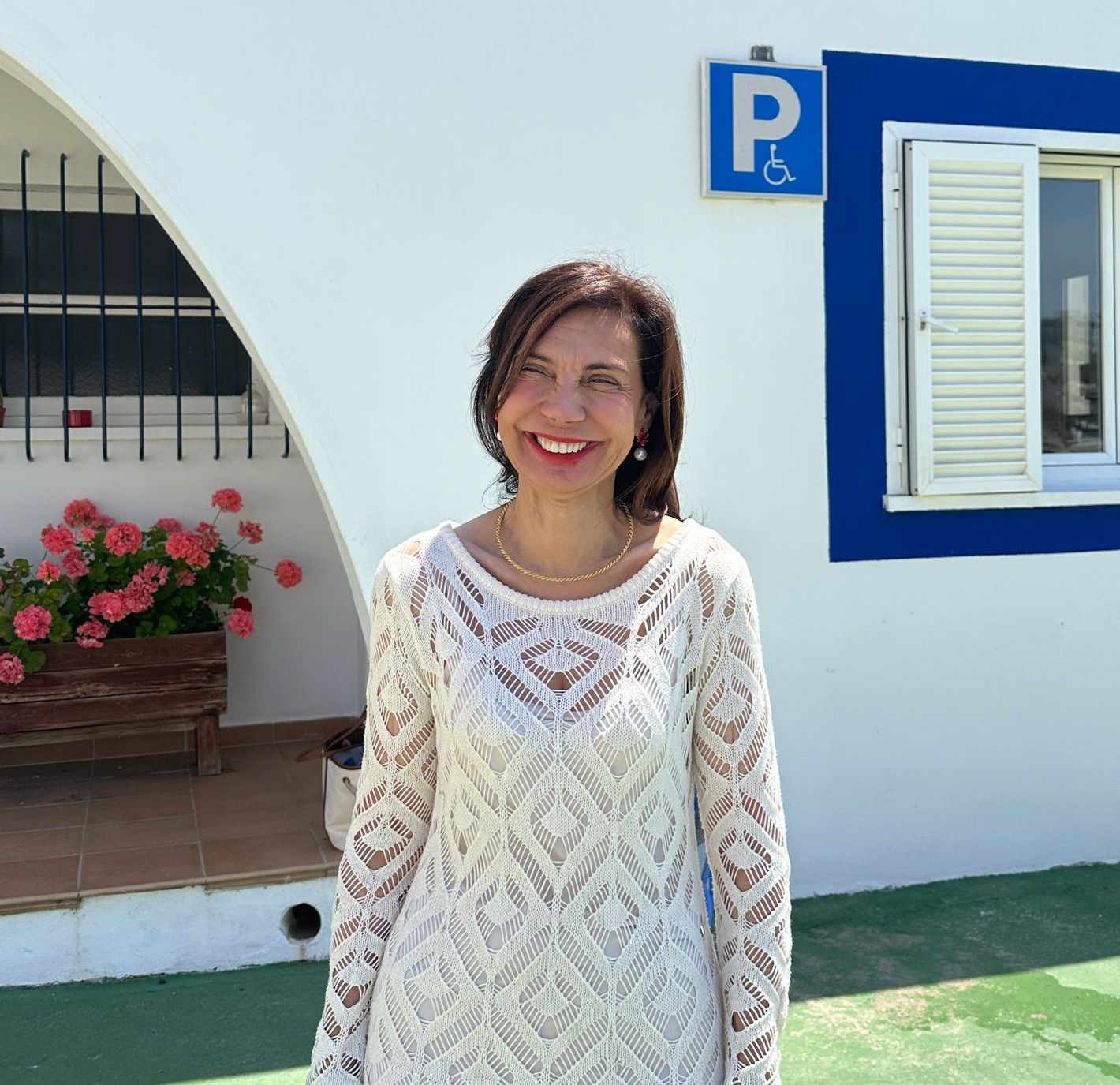 Una mujer vestida de blanco sonríe frente a una señal de estacionamiento para discapacitados