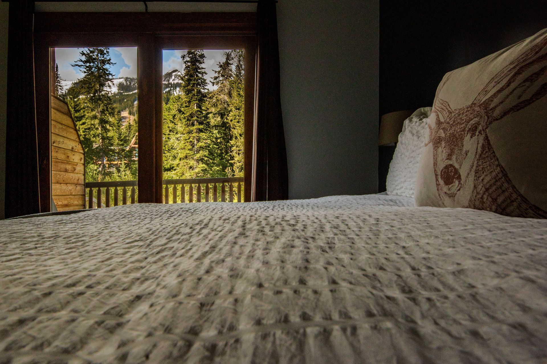 A bed with a view of a forest through a window.
