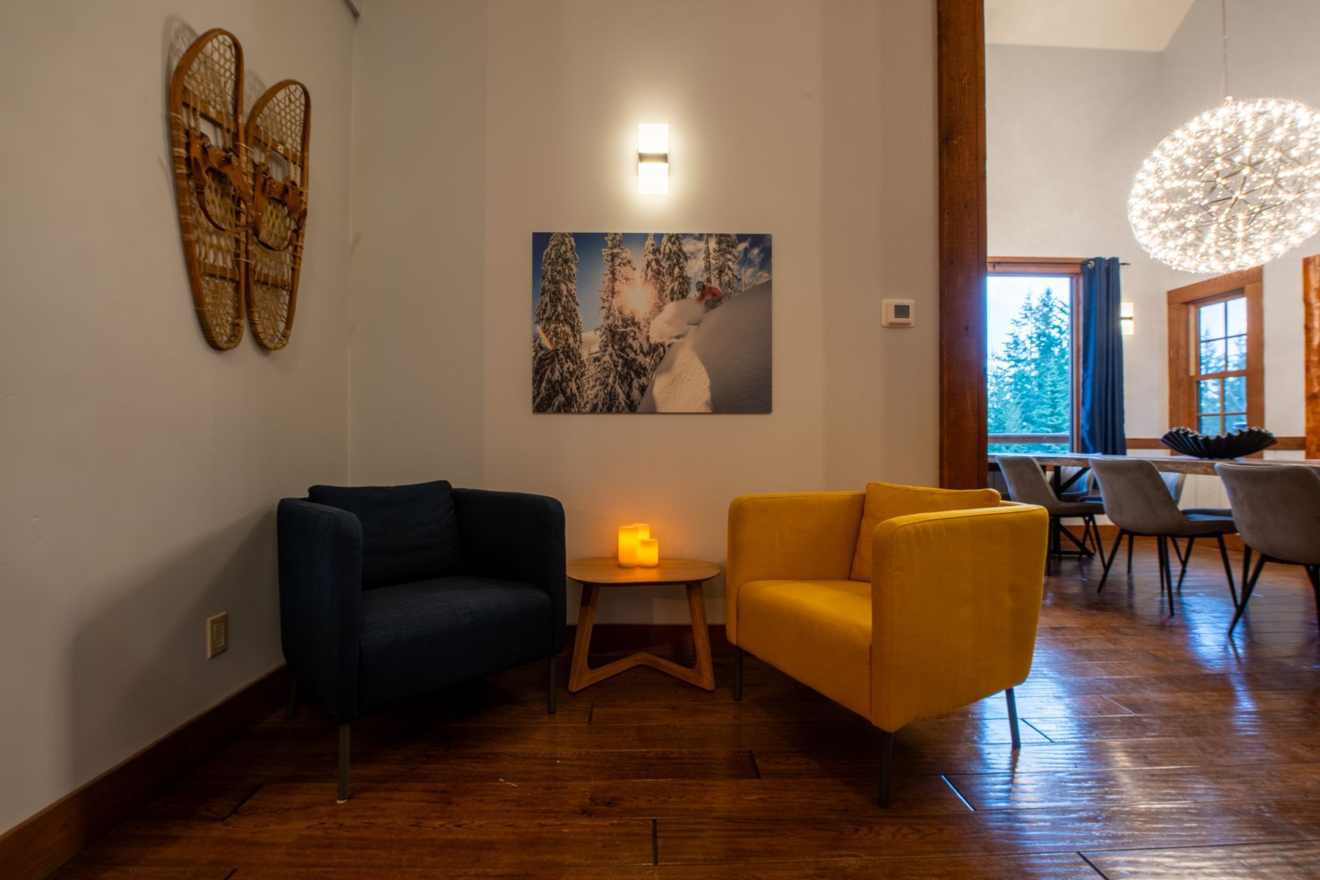 A living room with two chairs , a table and a painting on the wall.