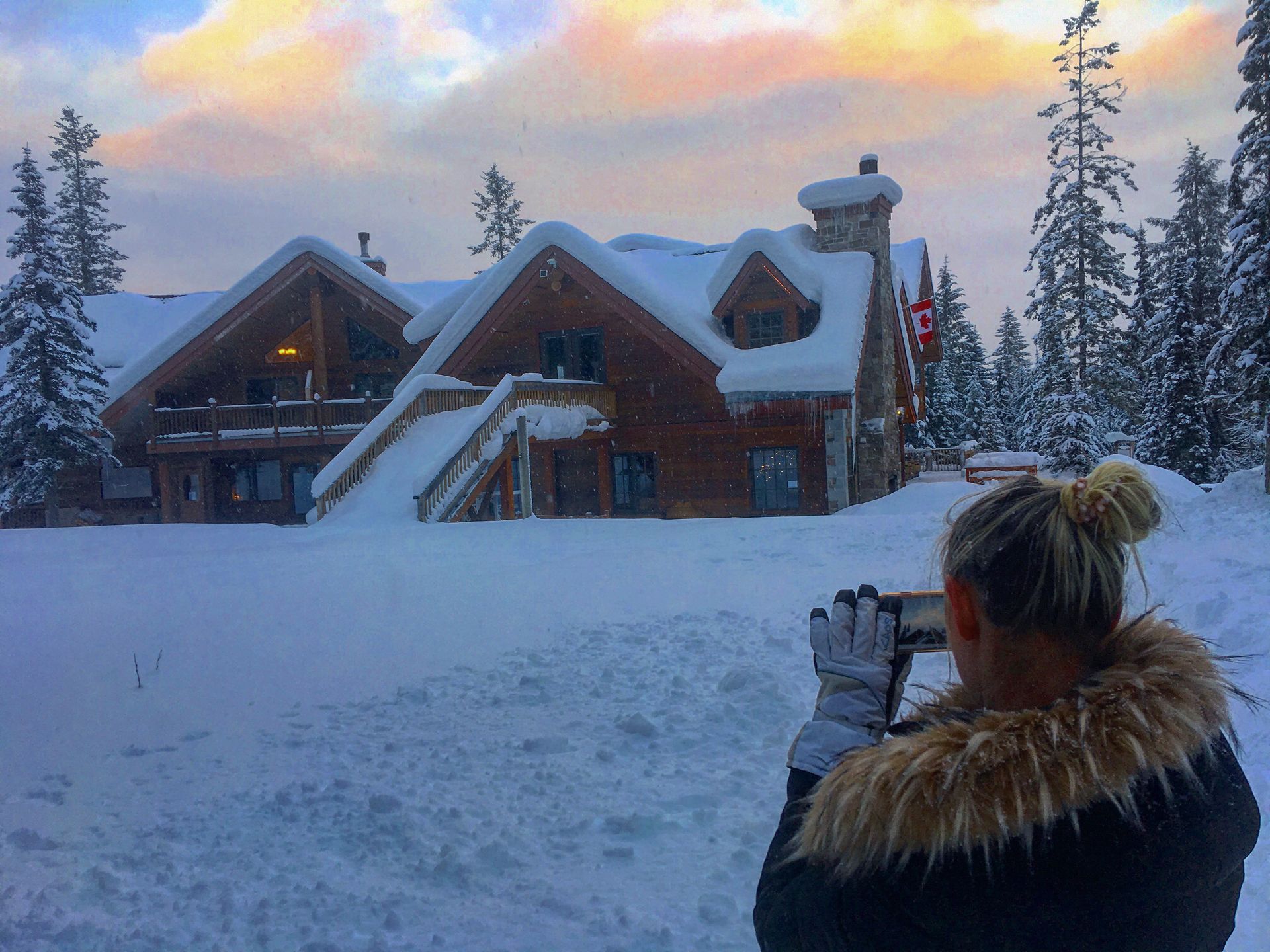 A woman is taking a picture of a house in the snow.