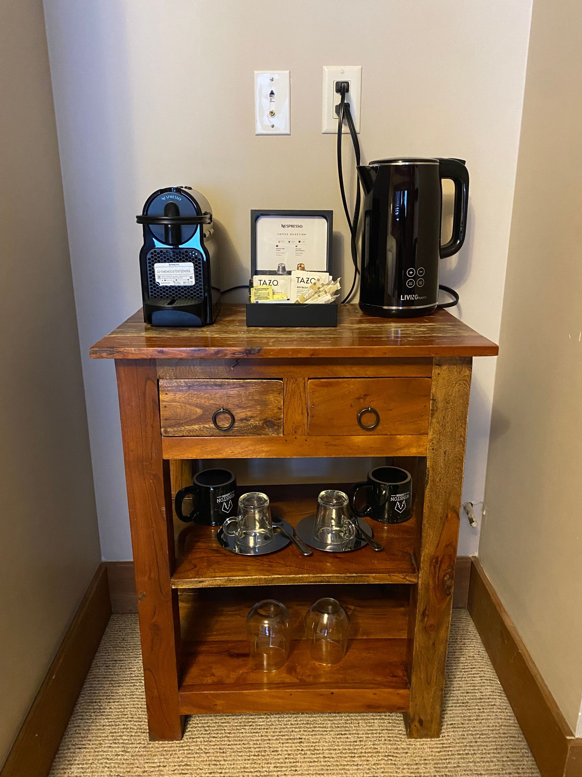 A wooden table with a coffee maker , kettle , cups and glasses on it.