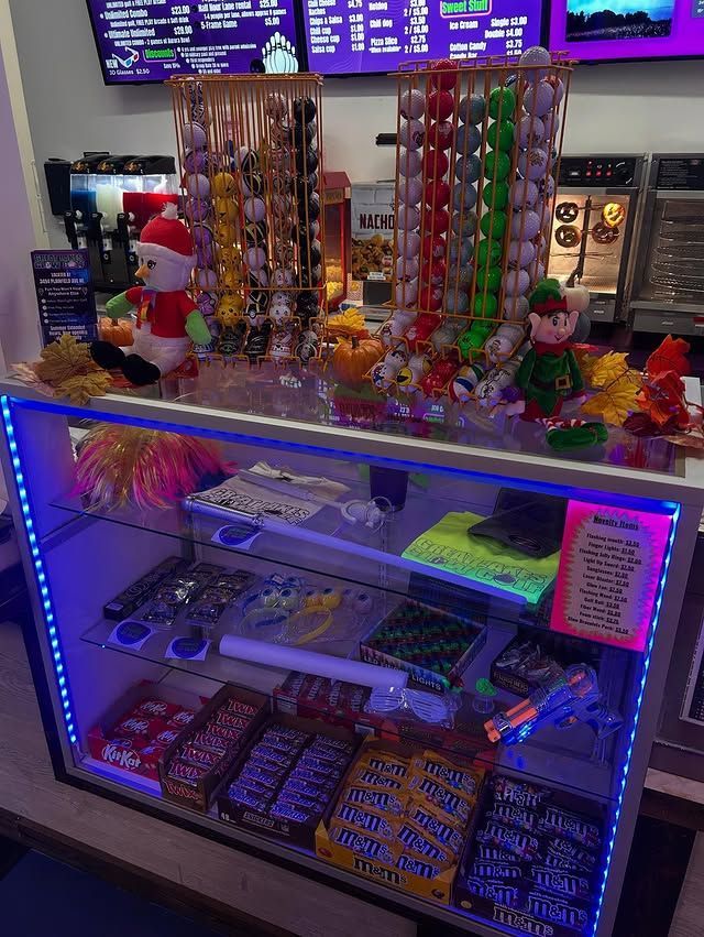 A glass concession display case featuring rows of colorful candy, illuminated by blue LED lights with festive decorations.
