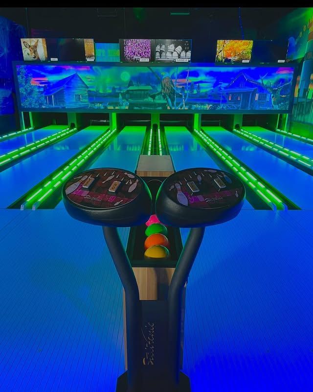 A dimly lit bowling alley with neon-green glowing lanes, screens above.