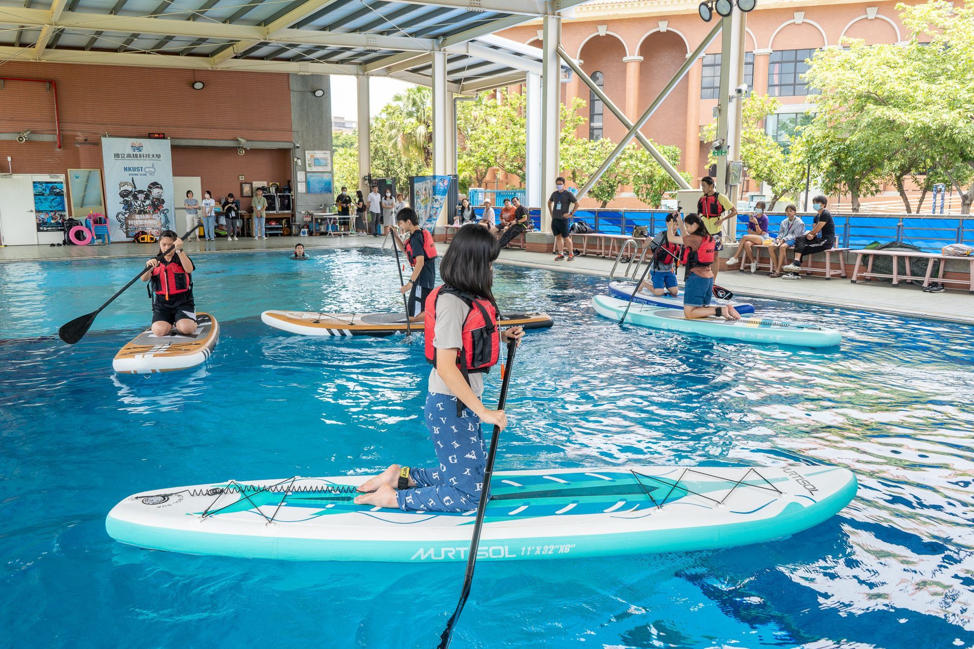 一群人正在泳池裡玩槳板。