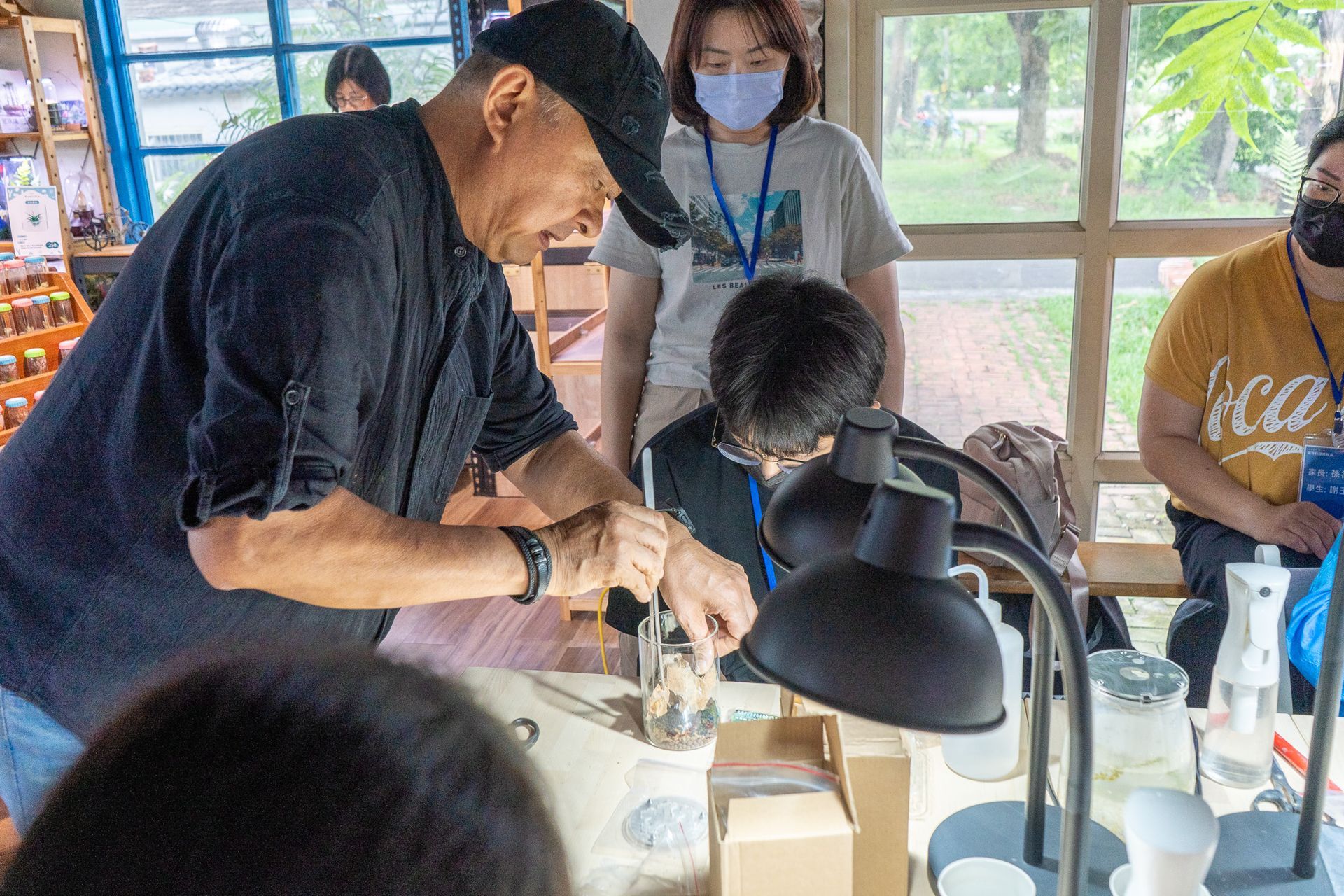 一名戴著黑帽子的男子正在加工一塊木頭，一群人圍觀。