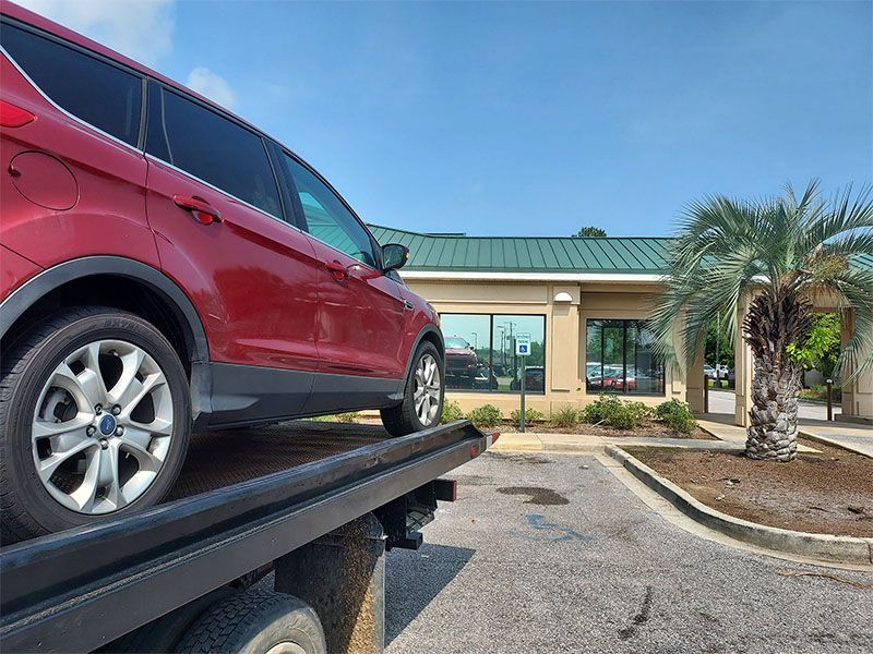 A red car is sitting on top of a tow truck.