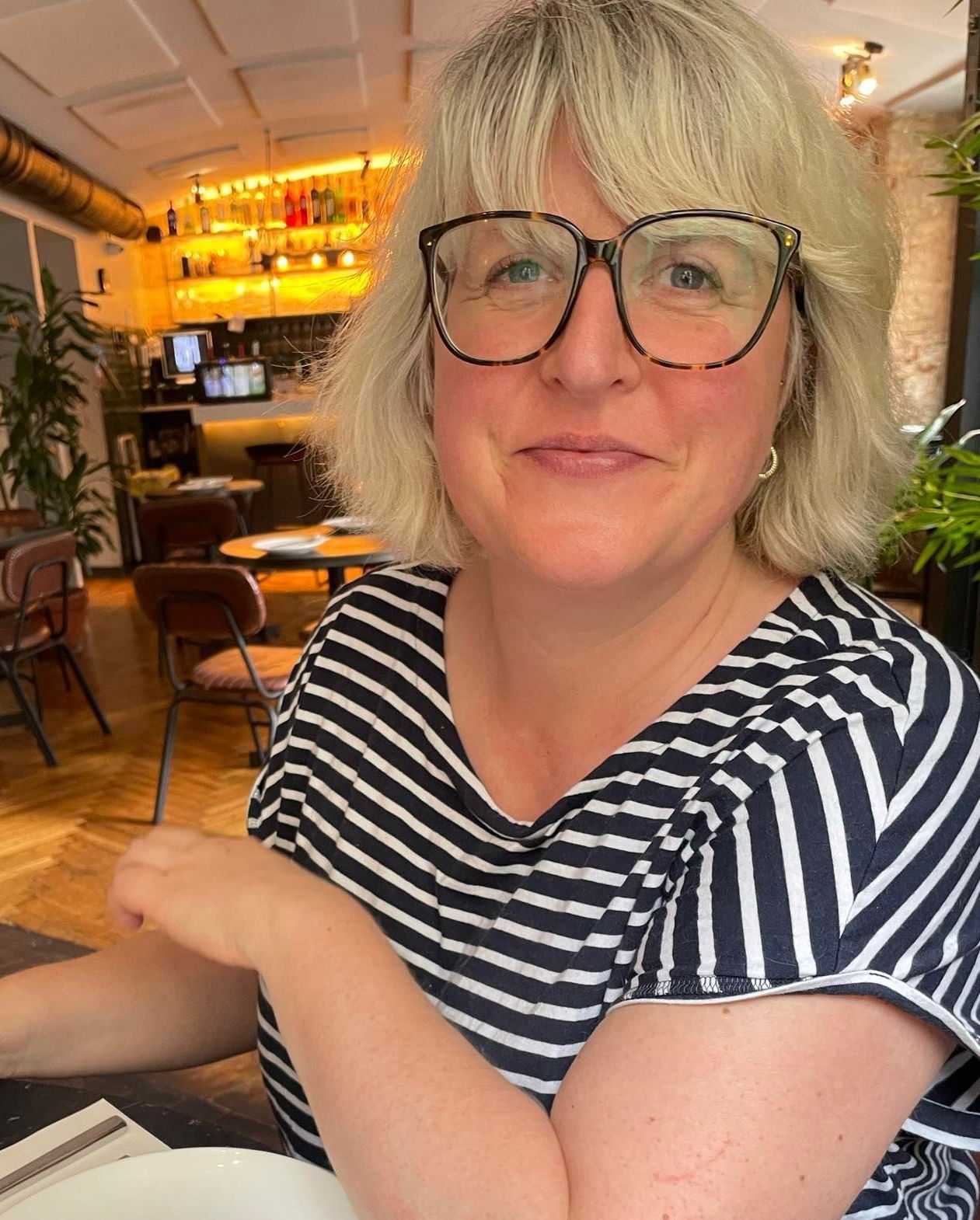 A woman wearing glasses and a striped shirt is sitting at a table in a restaurant.