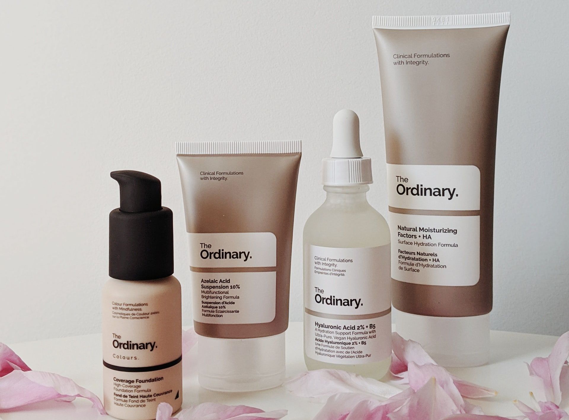 Three bottles of the ordinary cosmetics are sitting on a table surrounded by pink petals.