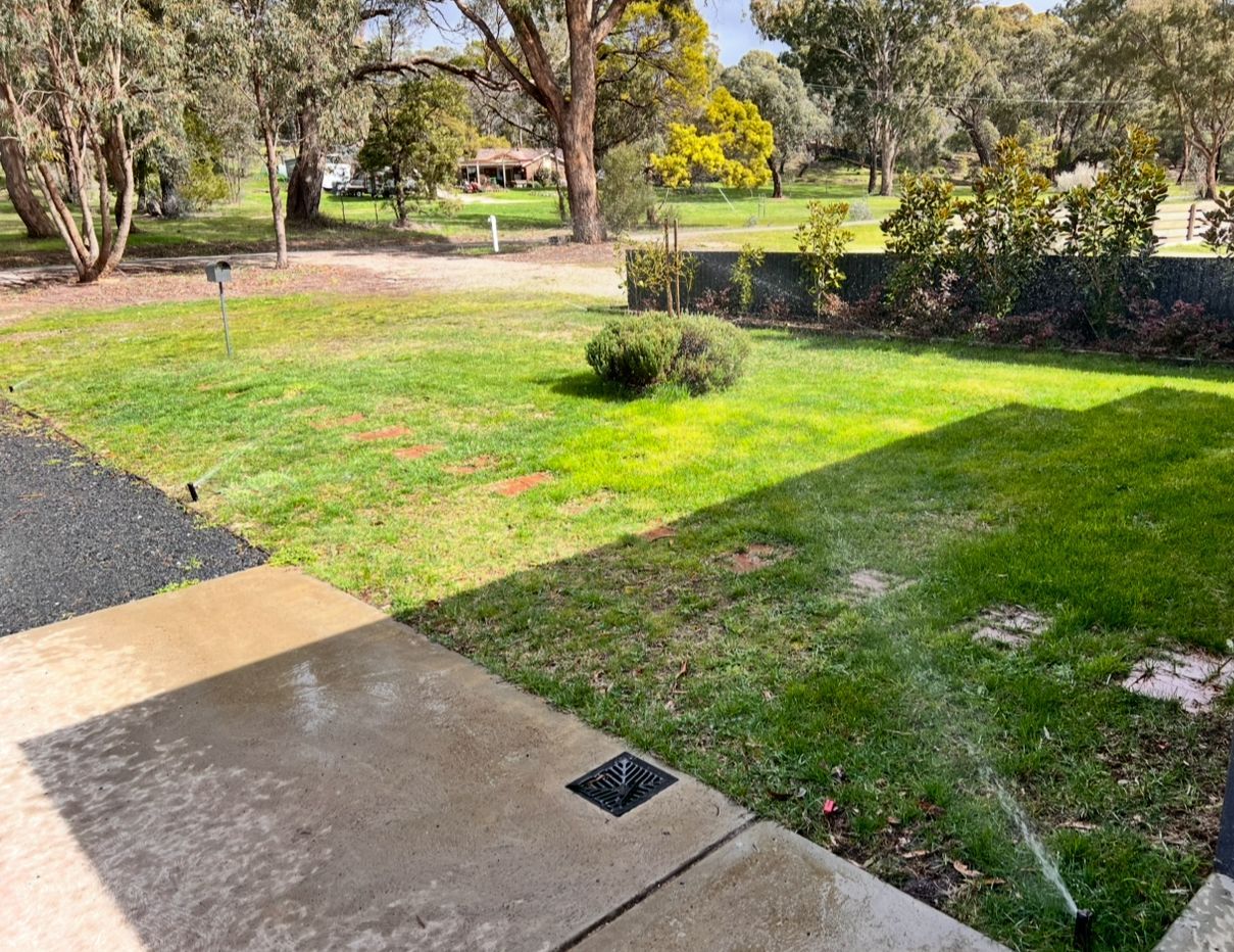 Lawn being watered by sprinklers; concrete patio in the foreground with trees in the background — Beaufort & District Earthworks in Beaufort, VIC