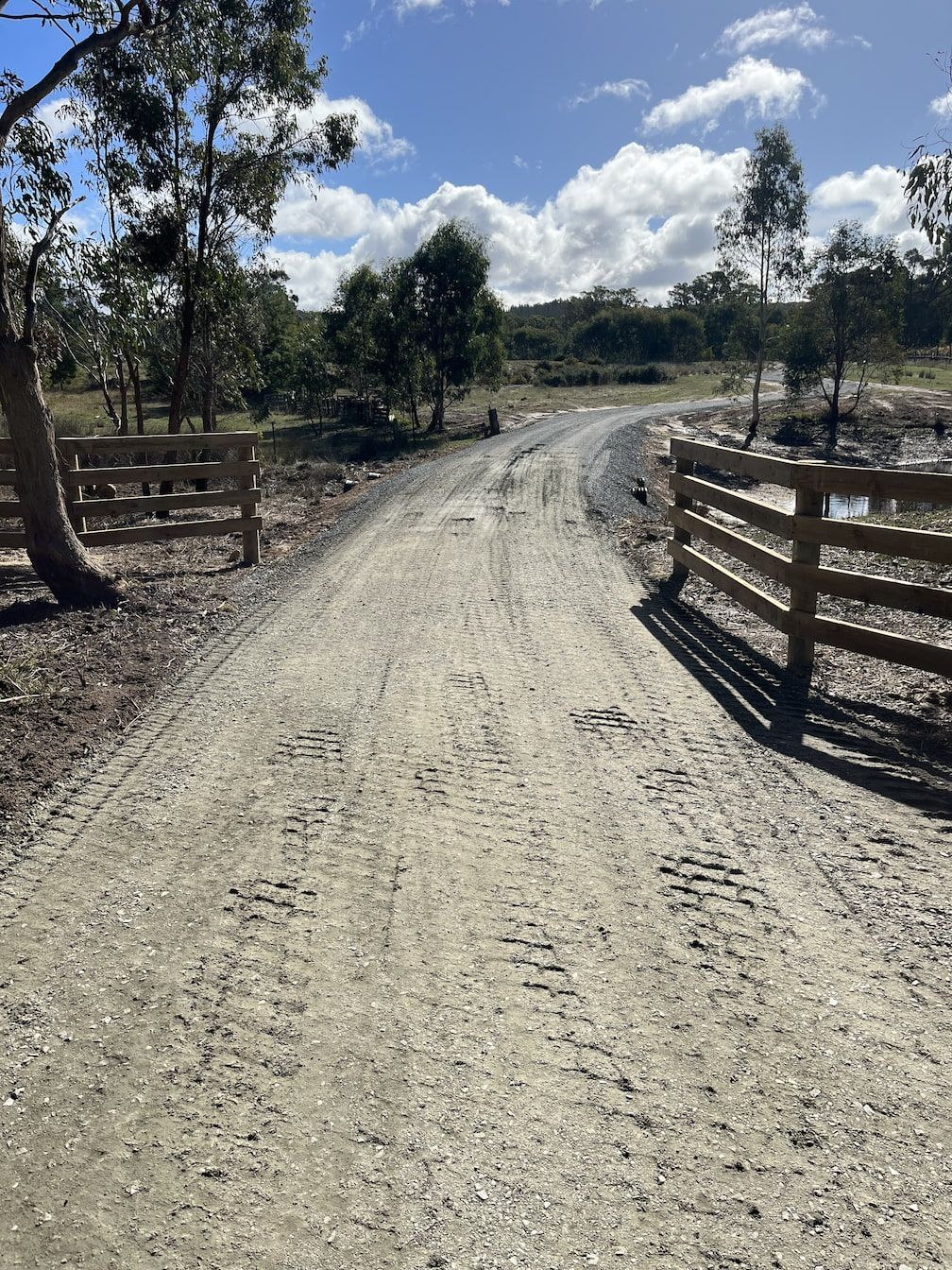 Dirt road with wooden fences and trees under a blue sky with puffy clouds — Beaufort & District Earthworks in Beaufort, VIC