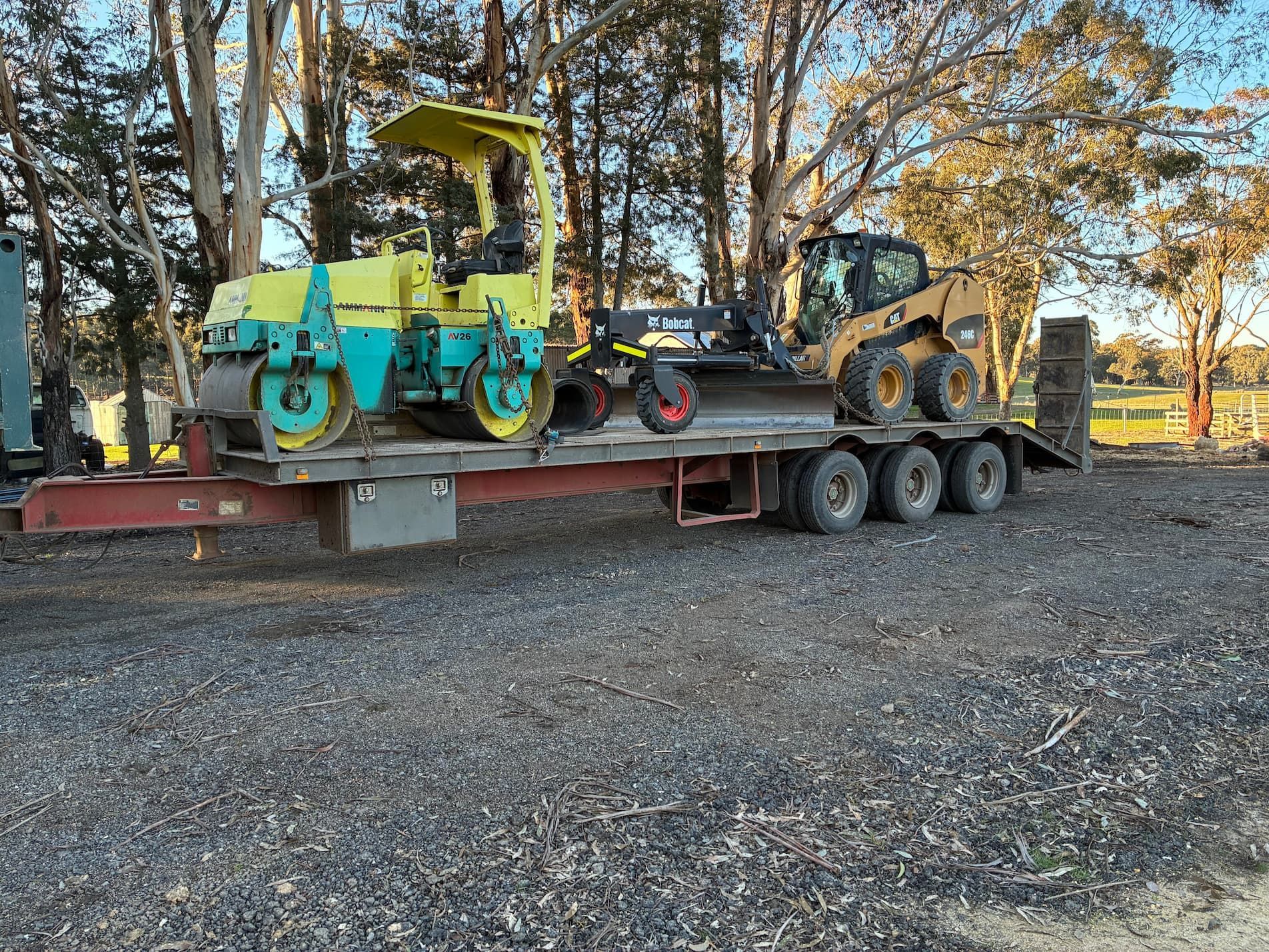 Yellow roller, Bobcat, and grader on a flatbed trailer outdoors — Beaufort & District Earthworks in Beaufort, VIC